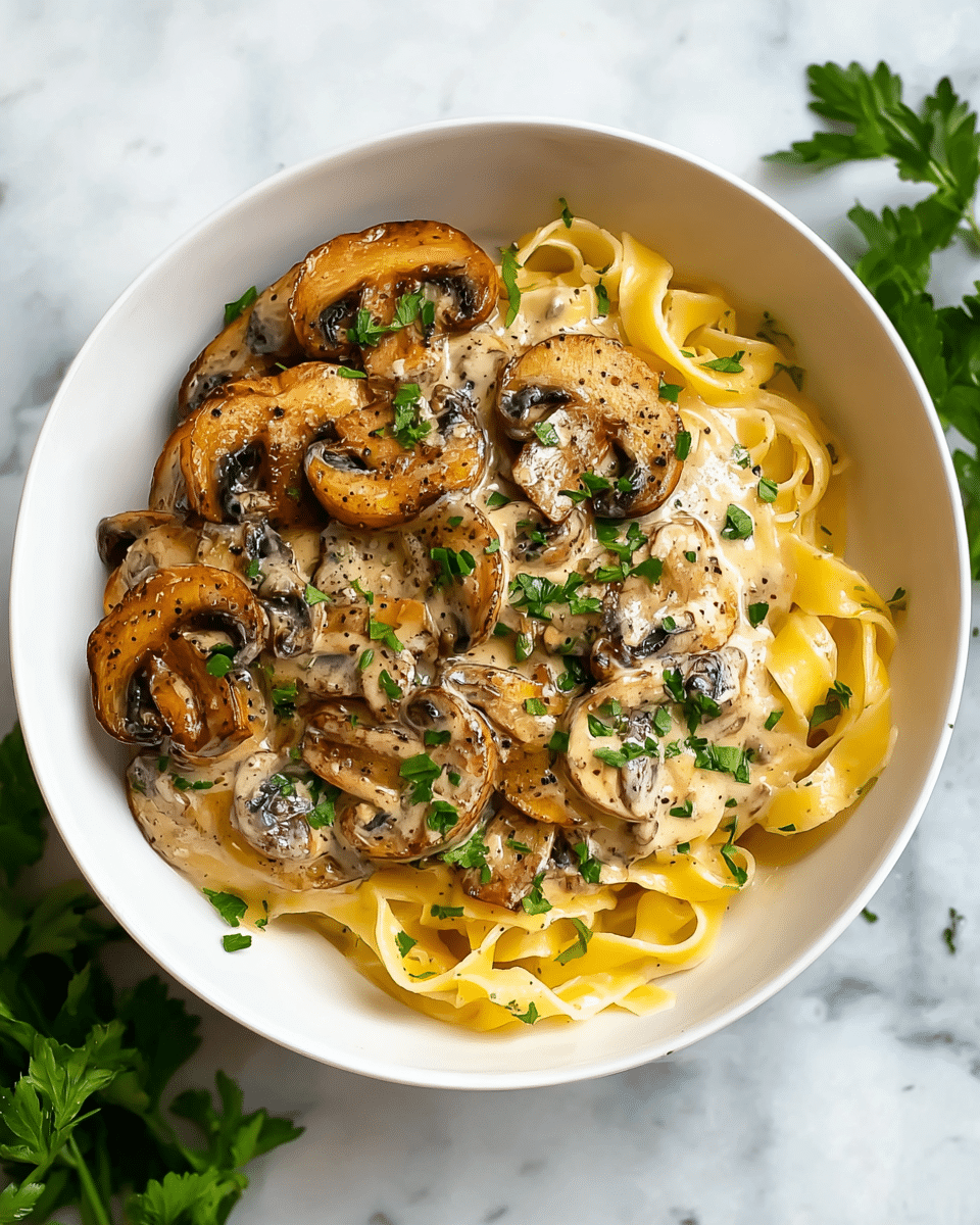 A white bowl filled with three main visible layers: at the bottom, there is a nest of wide, flat yellow pasta noodles with a smooth texture, lightly curled; above the pasta, there is a creamy beige sauce with a glossy surface coating the noodles; on top, there is a generous layer of sliced brown mushrooms, cooked to a golden-brown color with slightly darker edges, covered in sauce, sprinkled with small green parsley leaves and cracked black pepper. The bowl sits on a white marbled texture surface with some green parsley leaves around. Photo taken with an iphone --ar 4:5 --v 7