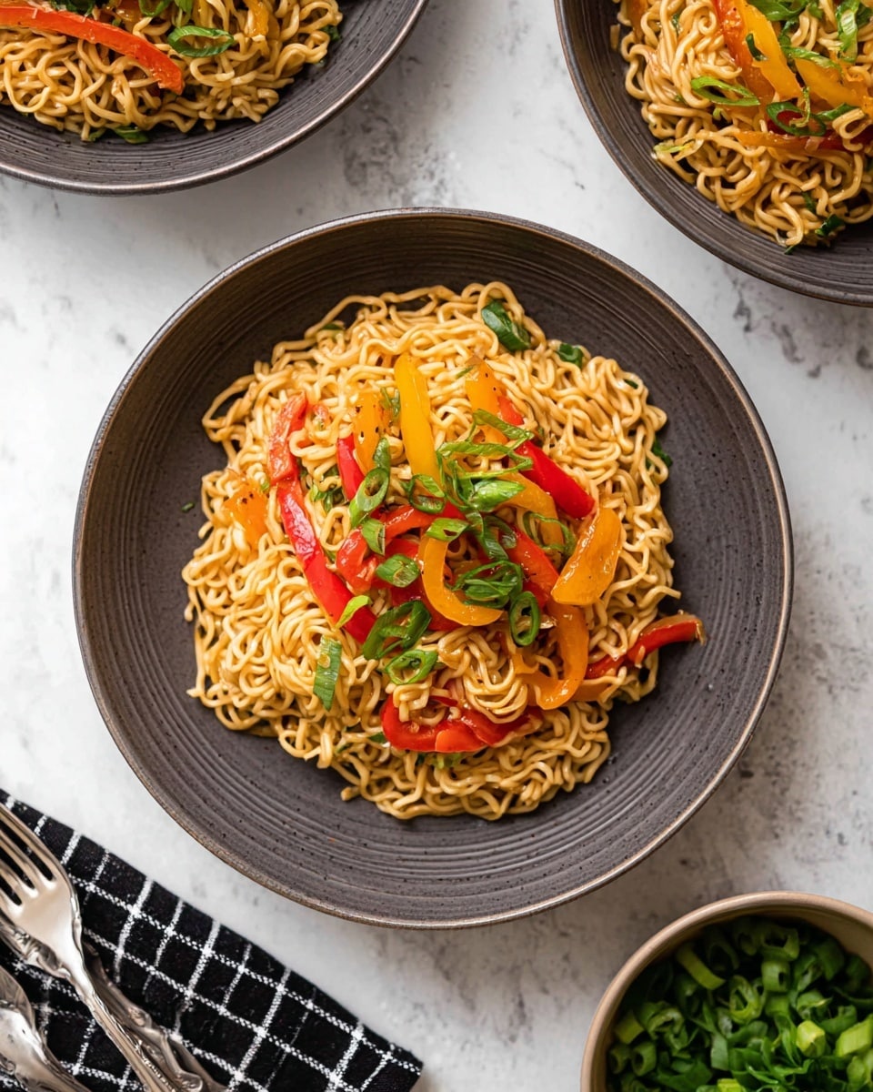 A bowl of cooked noodles with visible layers of light brown noodles mixed with thin slices of red and yellow bell peppers, lightly browned bits of cabbage, and topped with chopped green onions spread evenly across the dish. The noodles have a glossy and slightly oily texture, sitting in a deep white bowl placed on a white marbled surface. In the background, another similar bowl of noodles is partially visible with a small wooden bowl filled with chopped green herbs behind it, and the front part of an electric pressure cooker on the left side. A folded checkered cloth and a gold utensil are placed near the bowl. Photo taken with an iphone --ar 4:5 --v 7