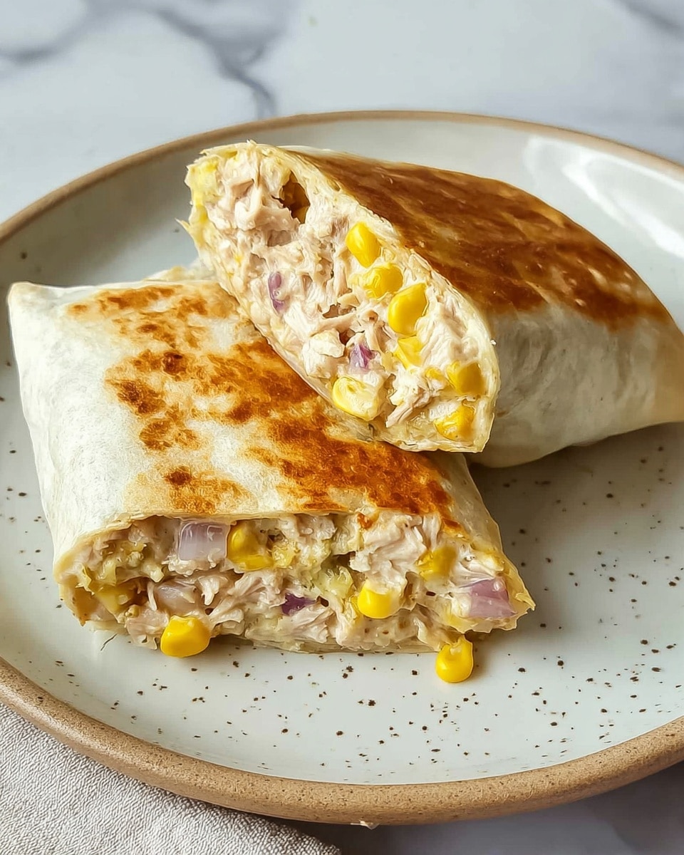Two halves of a toasted wrap are placed on a white speckled plate, set on a white marbled surface. The wrap is golden brown with a soft, slightly crispy texture. Inside, the filling has several visible layers: creamy light beige mixture with chunks of light pink tuna, bright yellow sweet corn, and small pieces of white onion mixed with bits of reddish-purple onion. The wrap is cut to show the filling clearly packed inside the soft, warm tortilla. photo taken with an iphone --ar 4:5 --v 7