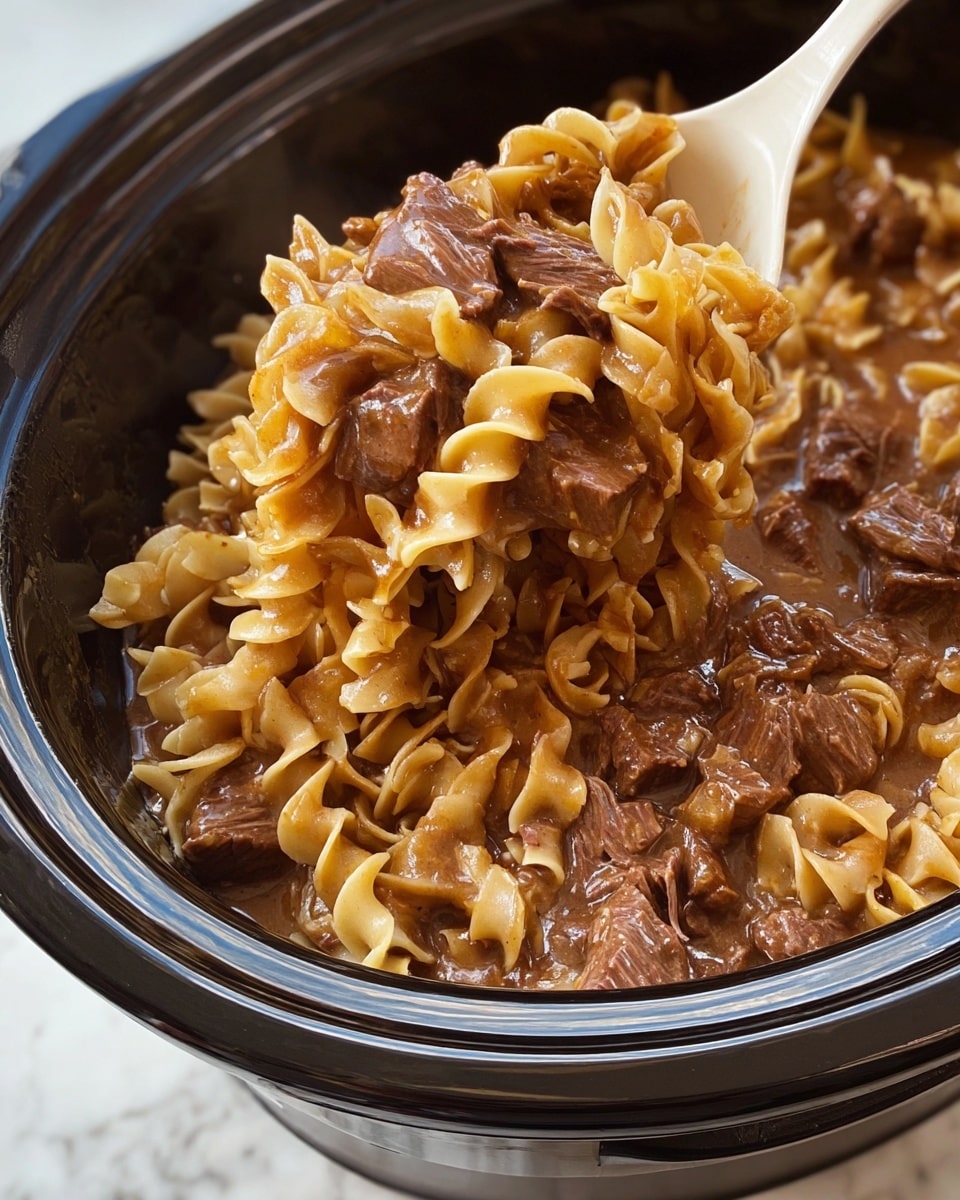 This image shows a close-up of a slow cooker filled with cooked egg noodles mixed with tender chunks and shreds of dark brown beef in a thick, glossy brown sauce, creating a rich and hearty texture. The noodles are soft and slightly curled, coated evenly with the sauce, while the beef pieces are scattered throughout, adding a chunky contrast. A white plastic spoon scoops a generous portion from the cooker, lifting the noodles and beef above the rest, showing the mixture’s moist and saucy consistency against the black inner pot. The whole scene is set on a white marbled surface. photo taken with an iphone --ar 4:5 --v 7