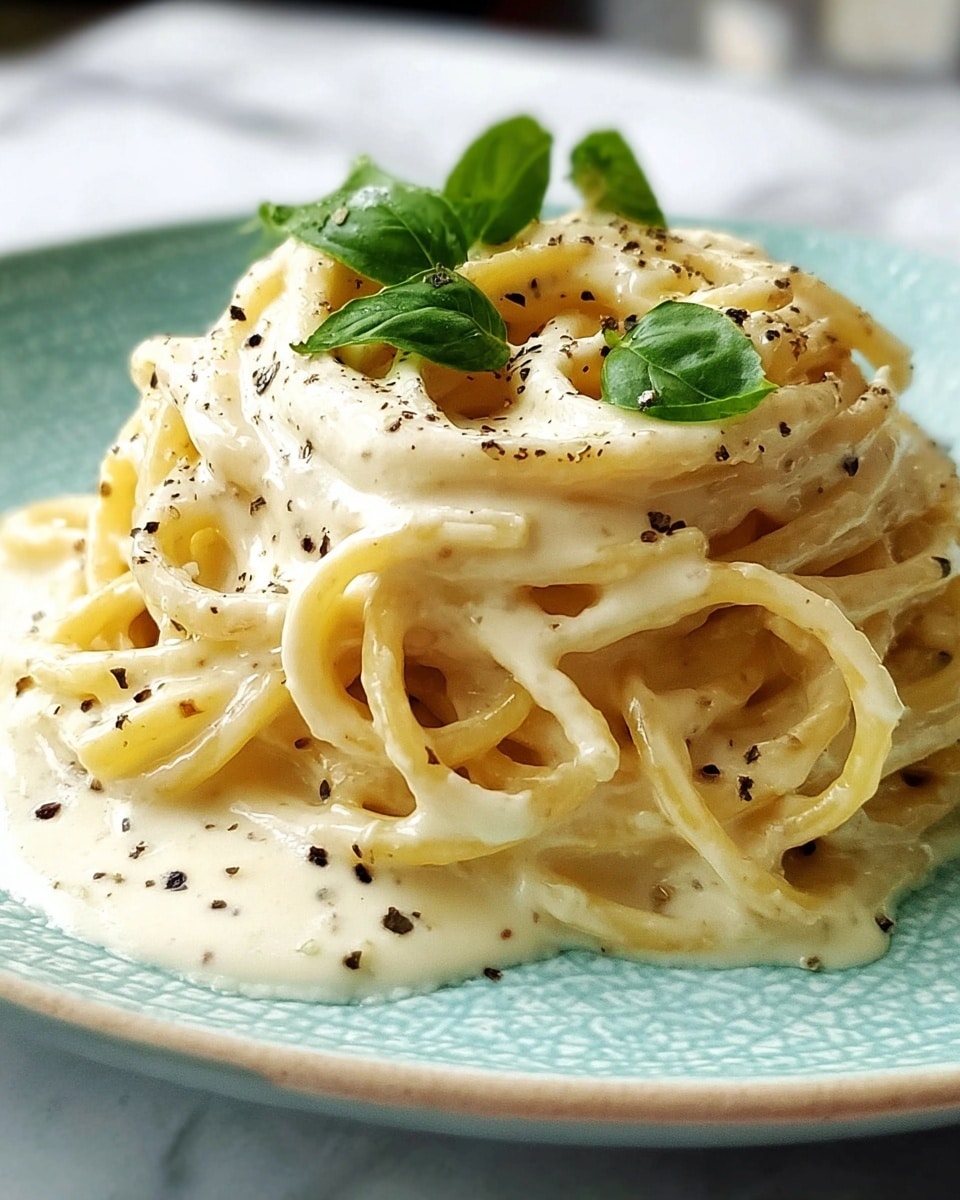 A close-up view of creamy pasta served on a white speckled plate, with one layer of thick, smooth spaghetti noodles coated evenly in a rich, light beige sauce, speckled with cracked black pepper and garnished with a few small fresh green basil leaves scattered on top, all set against a white marbled textured background. Photo taken with an iphone --ar 4:5 --v 7
