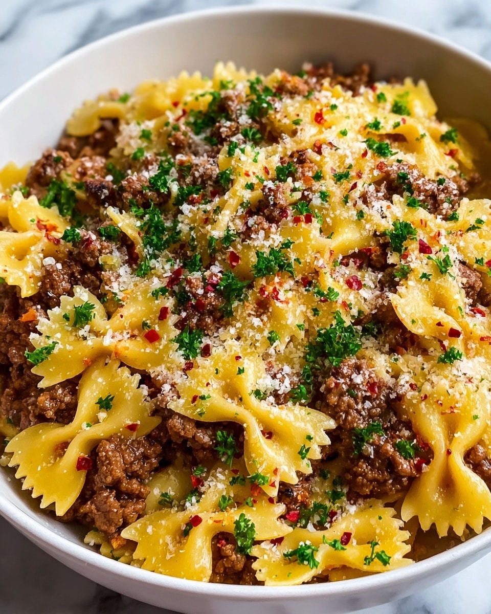 A close-up view of a white bowl full of farfalle pasta mixed with ground meat sauce, where the yellow pasta shapes have a smooth and slightly shiny texture, evenly coated with small brown crumbles of meat. The dish is sprinkled with finely chopped green herbs and small red chili flakes scattered on top. The sauce looks creamy and lightly coats the pasta without covering the meat or herbs completely. The bowl sits on a white marbled surface, enhancing the colors of the food. photo taken with an iphone --ar 4:5 --v 7