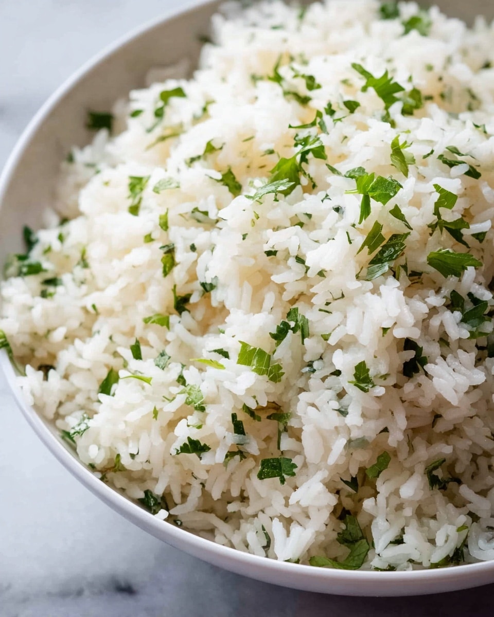 A close-up view of a white bowl filled with fluffy cooked white rice mixed with finely chopped fresh green herbs, scattered evenly throughout the rice grains. The rice looks soft and slightly shiny, with small green leaves adding a fresh, natural touch. The bowl sits on a white marbled surface, and the image focuses on the texture and details of the rice and herbs. Photo taken with an iphone --ar 4:5 --v 7