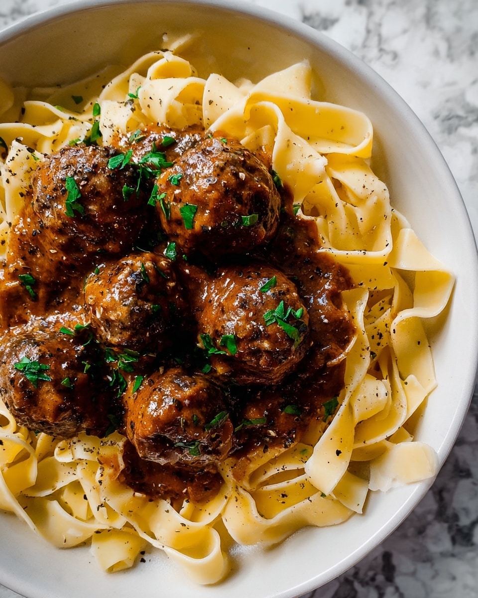 A white plate holds a bed of pale yellow fettuccine pasta arranged loosely in a circle. On top sit six round meatballs covered in a thick, brown sauce, glistening with moisture and sprinkled with small green parsley leaves for color contrast. A woman's hand with red nail polish holds a fork and knife, cutting into one of the meatballs at the front center of the plate. The scene is set on a dark wooden textured surface with a mustard-yellow cloth napkin folded in the upper left corner. photo taken with an iphone --ar 4:5 --v 7