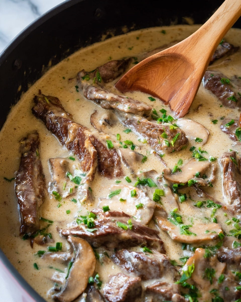 The image shows a close-up of a creamy dish with several layers of brown cooked meat slices mixed with light brown mushroom slices, all covered in a smooth, thick beige sauce. Bright green chopped herbs are scattered on top, adding fresh color. A wooden spoon is seen stirring the dish inside a dark pan. The sauce has a slightly glossy texture and lumps of meat and mushrooms are clearly visible. The setting is on a white marbled surface. photo taken with an iphone --ar 4:5 --v 7