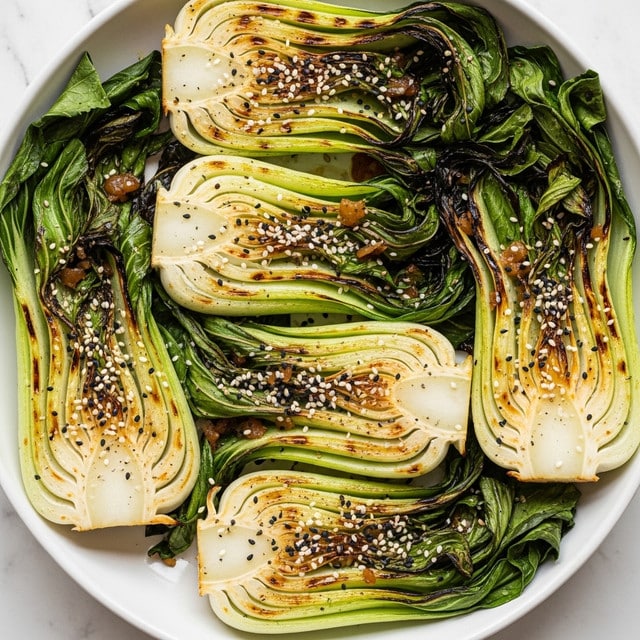 The dish shows several halves of grilled bok choy placed side by side in a white bowl, each half revealing layered pale green to light golden stalks with charred grill marks and crispy edges, topped with small white and black sesame seeds. The bok choy leaves surrounding the stalks are deep green and slightly wilted. There are some visible caramelized bits and a light seasoning of black pepper on the surface of the bok choy. The bowl sits on a white marbled texture. Photo taken with an iphone --ar 4:5 --v 7