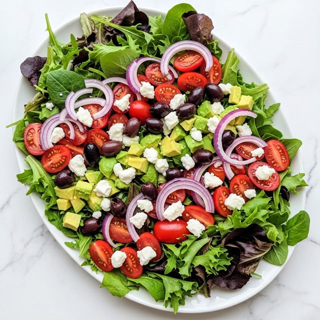 The image shows a fresh salad on a white oval plate placed on a white marbled surface. The salad has several layers, starting with a base of mixed green and purple lettuce leaves that are leafy and textured, spread evenly over the plate. On top of the greens, bright red cherry tomato halves are scattered, adding a smooth, shiny contrast. Thin slices of pale purple onion are layered lightly over the tomatoes. Small chunks of light green avocado pieces are spread intermittently, providing a soft texture and creamy look. Dark black olives are placed sporadically throughout the salad, along with small crumbles of white feta cheese that add a rough texture and bright contrast. The ingredients are fresh and vibrant, showing a mix of smooth, juicy, and leafy textures. photo taken with an iphone --ar 4:5 --v 7