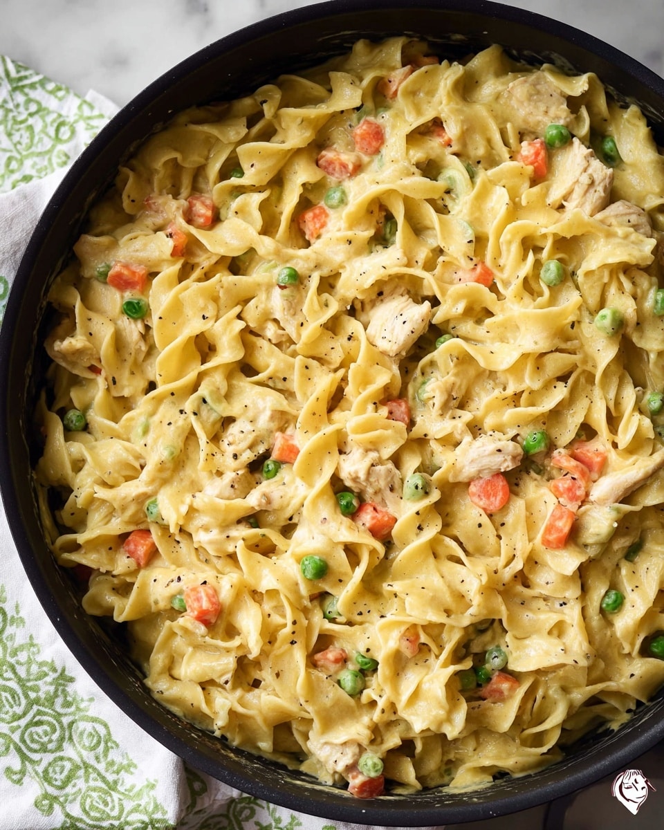 A close-up view of creamy pasta with three layers: the base layer is creamy sauce with a smooth, pale yellow texture; the middle layer consists of twisted, soft egg noodles in a light yellow color; the top layer has small chunks of orange carrots, green peas, and shredded pieces of white chicken mixed evenly throughout, all coated in the creamy sauce. The pasta is inside a black skillet, placed on a white marbled surface, with a white and green checkered cloth nearby. photo taken with an iphone --ar 4:5 --v 7