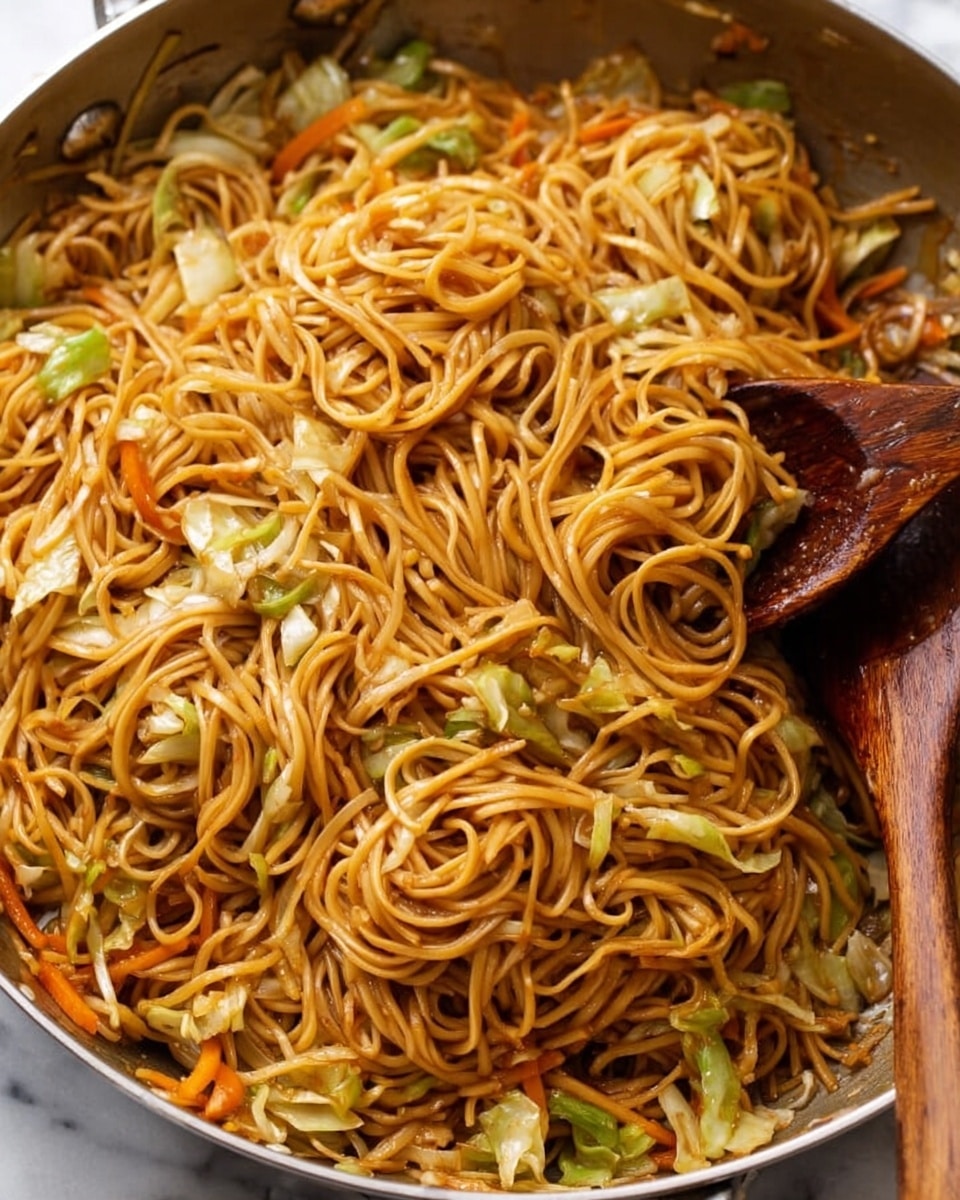 A large silver pan is filled with a tangle of thin, dark golden-brown noodles mixed with scattered small pieces of light green cabbage. The noodles have a slight shine, showing they are well coated with sauce, and are spread evenly across the pan's surface. Two wooden spoons rest in the pan, one leaning on the side and the other partially submerged in the noodles. The background has a white marbled texture, and a striped towel is visible at the bottom edge. photo taken with an iphone --ar 4:5 --v 7