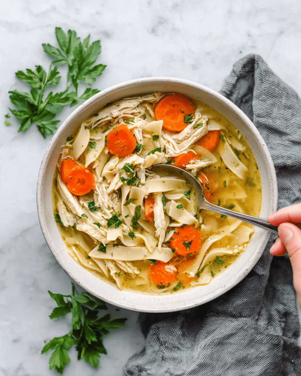 A white pot filled with chicken soup on a white marbled surface. The soup shows several layers: shredded white chicken pieces on top, orange carrot slices and light-yellow onion slices beneath, all floating in a clear golden broth. Green herbs are sprinkled over the soup, adding small bright green specks. A spoon is partially inside the soup, and a gray cloth is near the pot. Nearby are white plates with silver cutlery and a small white bowl with pepper seeds. Photo taken with an iphone --ar 4:5 --v 7
