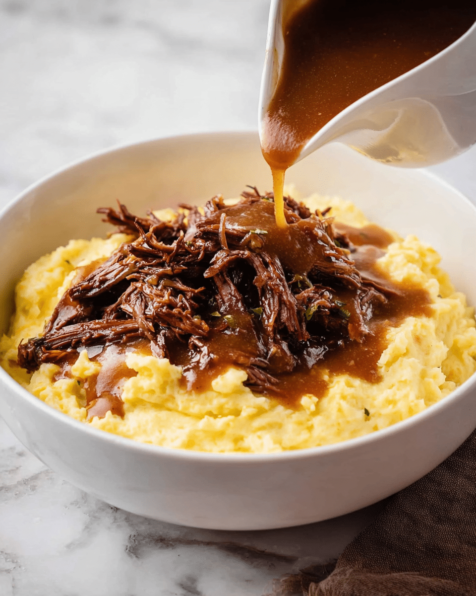 A white bowl holds a creamy light yellow base of mashed potatoes with visible small lumps and herbs mixed in. On top, there is a generous pile of dark brown shredded beef with a slightly crispy texture on some edges. A stream of rich, smooth brown gravy is being poured from a white gravy boat onto the beef, creating a glossy coating that flows slowly over the meat and onto the potatoes. The background is a white marbled surface, enhancing the warm colors of the dish. photo taken with an iphone --ar 4:5 --v 7