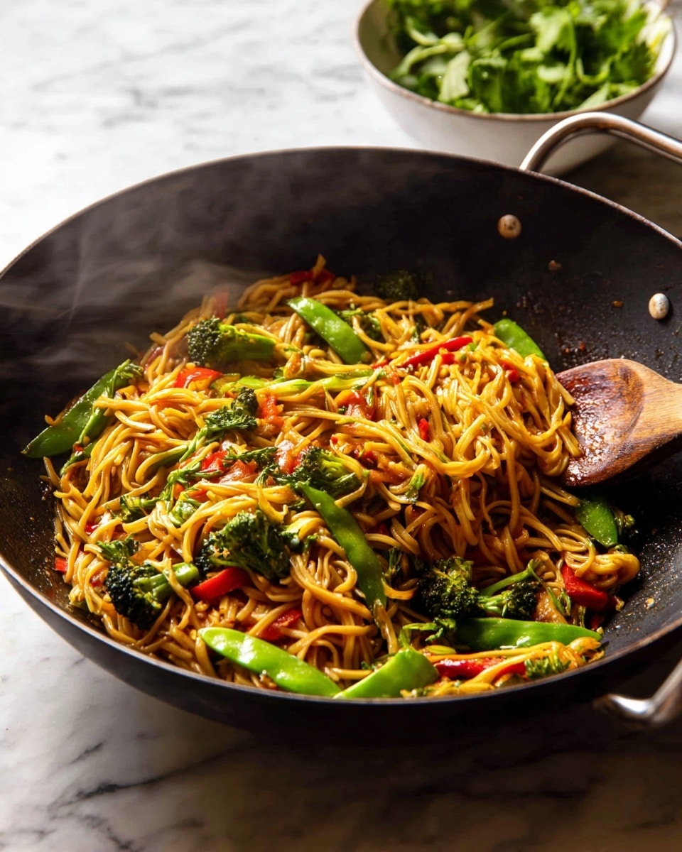 A black wok filled with stir-fried noodles sits on a white marbled surface, steaming hot. The dish has three main layers: a base of golden-yellow noodles that look soft and glossy, mixed with bright green snap peas scattered throughout. On top and mixed in, there are small, vibrant red pieces of bell pepper and dark green broccoli florets. A wooden spoon is partially submerged in the noodles, lifting some strands at the back right of the wok. In the background, a white bowl with fresh green herbs adds a touch of brightness. photo taken with an iphone --ar 4:5 --v 7