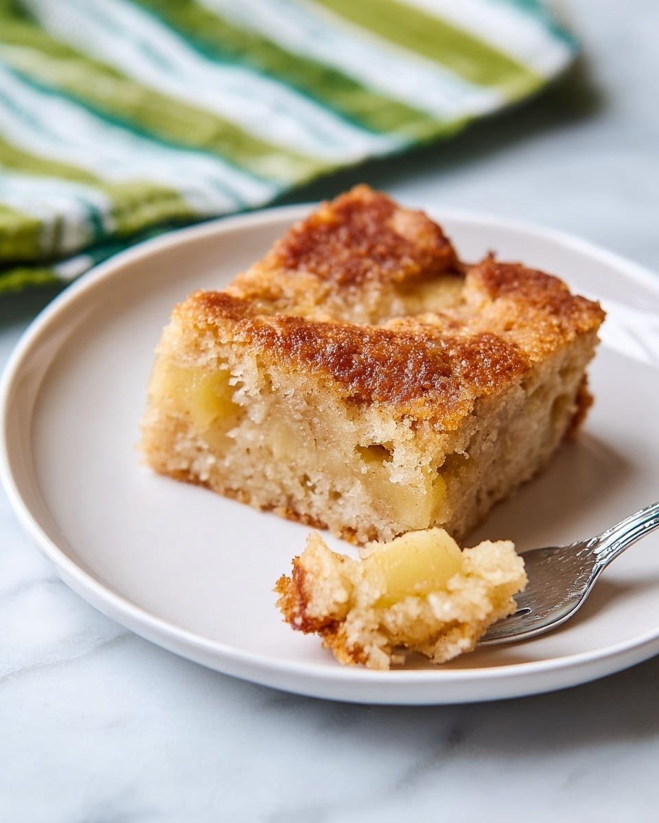 A close-up view of a baked apple cake in a square metal baking pan with four large pieces cut from it. The cake has two main layers: the bottom layer is light brown with visible soft yellow apple chunks mixed inside, and the top layer is a golden brown crumbly crust with a sugary texture. The top looks slightly crisp and uneven with small crunchy bits. The pan is placed on a white marbled surface. photo taken with an iphone --ar 4:5 --v 7