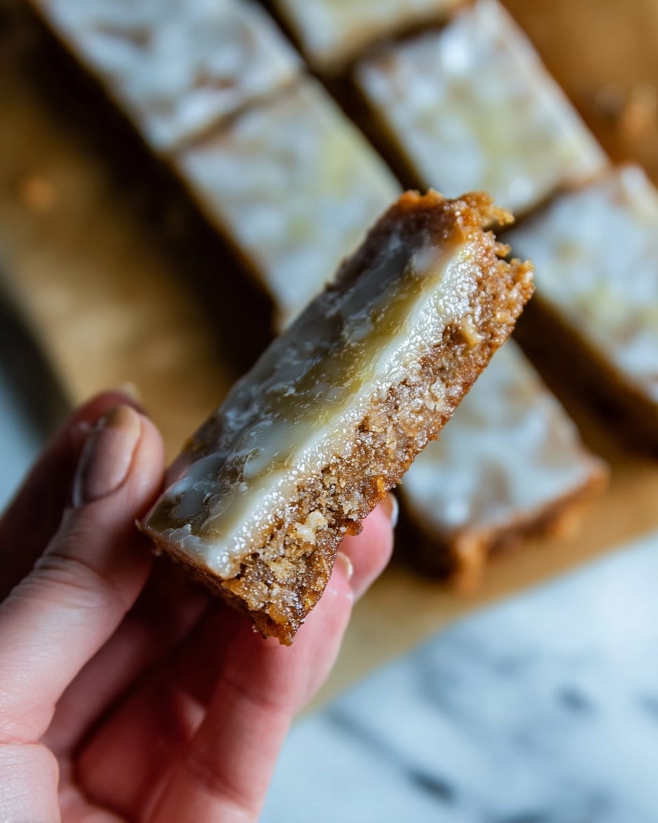 The image shows rows of rectangular cake bars with a dark brown base layer topped with a thin, uneven light grayish glaze layer. Each bar is neatly cut, revealing a dense and slightly crumbly texture in the base, with the glaze having a shiny, cracked finish on top. The bars are arranged on a light brown parchment paper that rests on a white marbled surface. photo taken with an iphone --ar 4:5 --v 7