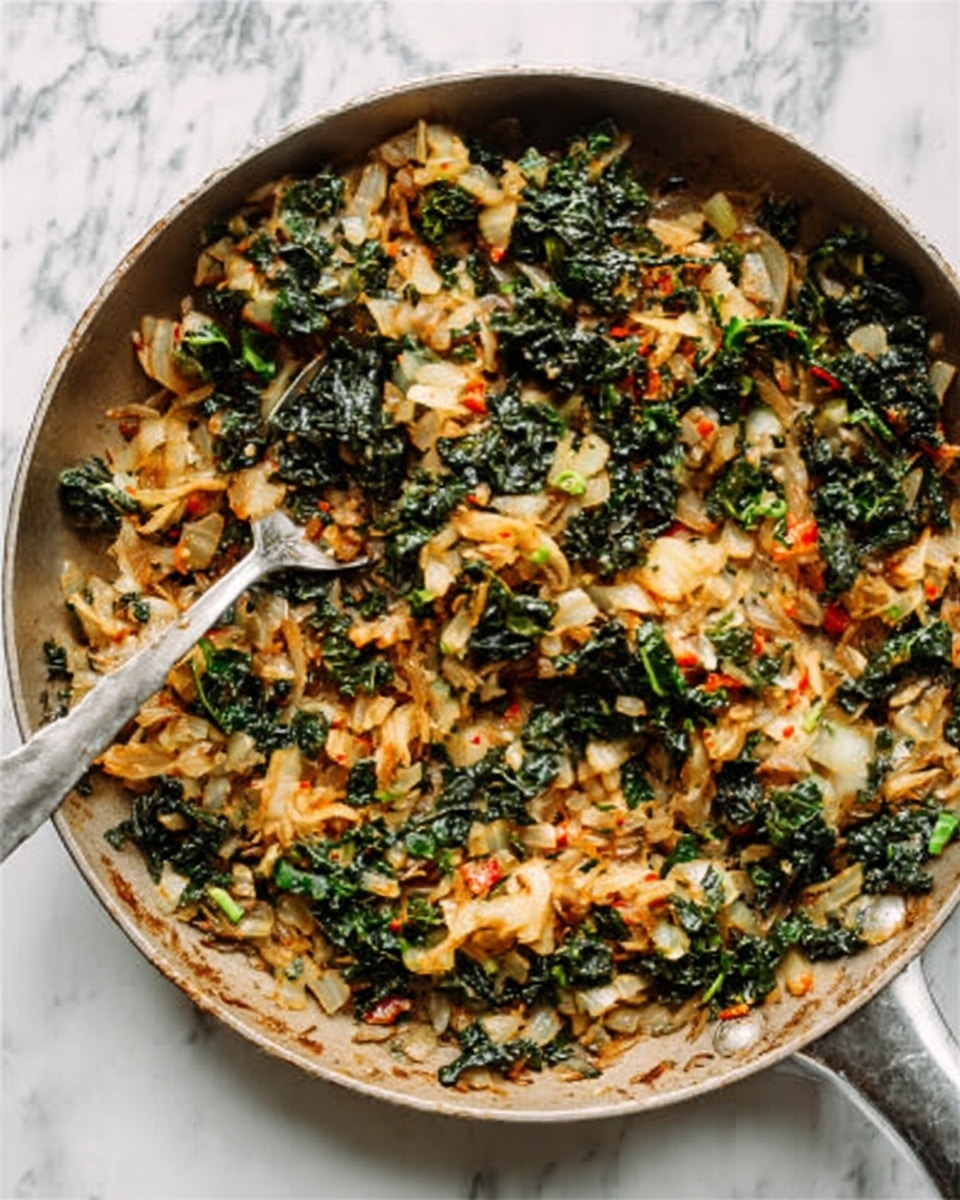 The dish is served in a white scalloped bowl, filled with cooked vegetables in two main layers: the base layer contains wilted dark green kale leaves with a slightly rough texture, mostly at the bottom and sides, while the top layer has soft, chunky pieces of light yellow to golden brown cabbage with some caramelized edges. The vegetables are mixed with small bits of red chili flakes and sprinkled with tiny green herb flakes. A silver spoon is placed inside the bowl on the left side, and the bowl sits on a white marbled surface with a grey cloth napkin partially visible under the bowl's right edge. Photo taken with an iphone --ar 4:5 --v 7
