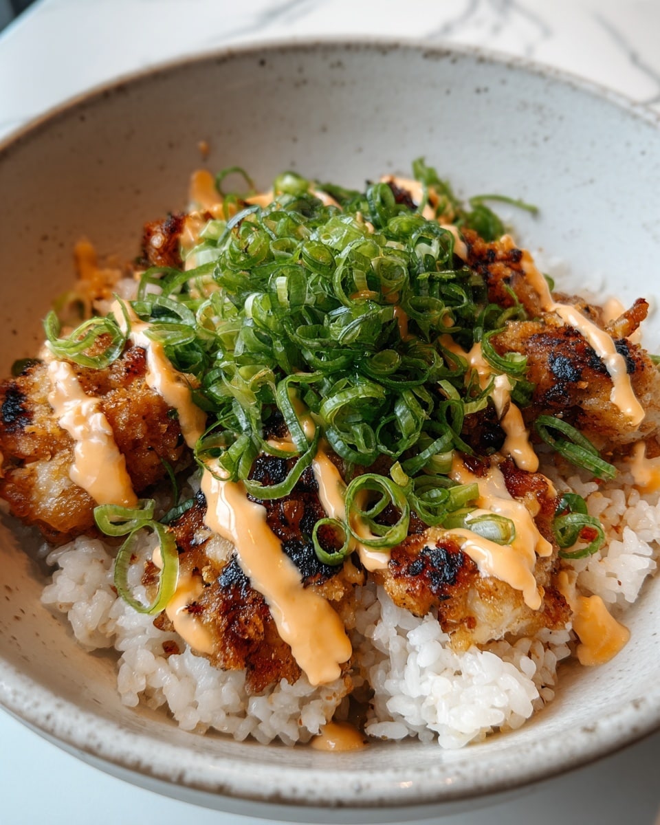 A white bowl with a base layer of cooked white rice topped with several golden-brown fried pieces of chicken or fish, each piece showing some crispy edges and char marks. On top of the fried pieces, there is a generous drizzle of light orange creamy sauce in zigzag lines. Fresh chopped green onions are sprinkled over the sauce and protein, adding a bright green color and a fresh texture contrast. The bowl sits on a white marbled surface. photo taken with an iphone --ar 4:5 --v 7