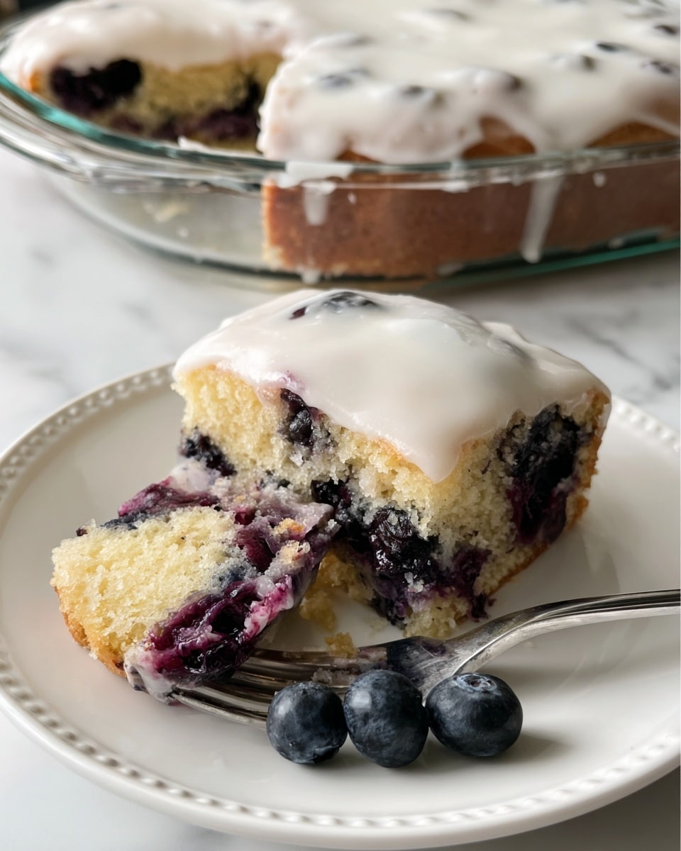 The image shows a close-up of a rectangular slice of blueberry cake on a white marbled surface with other cake pieces nearby. The cake has two layers: the bottom layer is light yellow and spongy, filled with scattered dark blue blueberries that look juicy and soft; the top layer has a light brown crumbly texture with some white thin drizzle over it. The blueberries inside the cake create small bursts of deep blue and purple against the pale yellow sponge. The edges of the cake are slightly crumbly and golden brown, showing a fresh baked look. Photo taken with an iphone --ar 4:5 --v 7