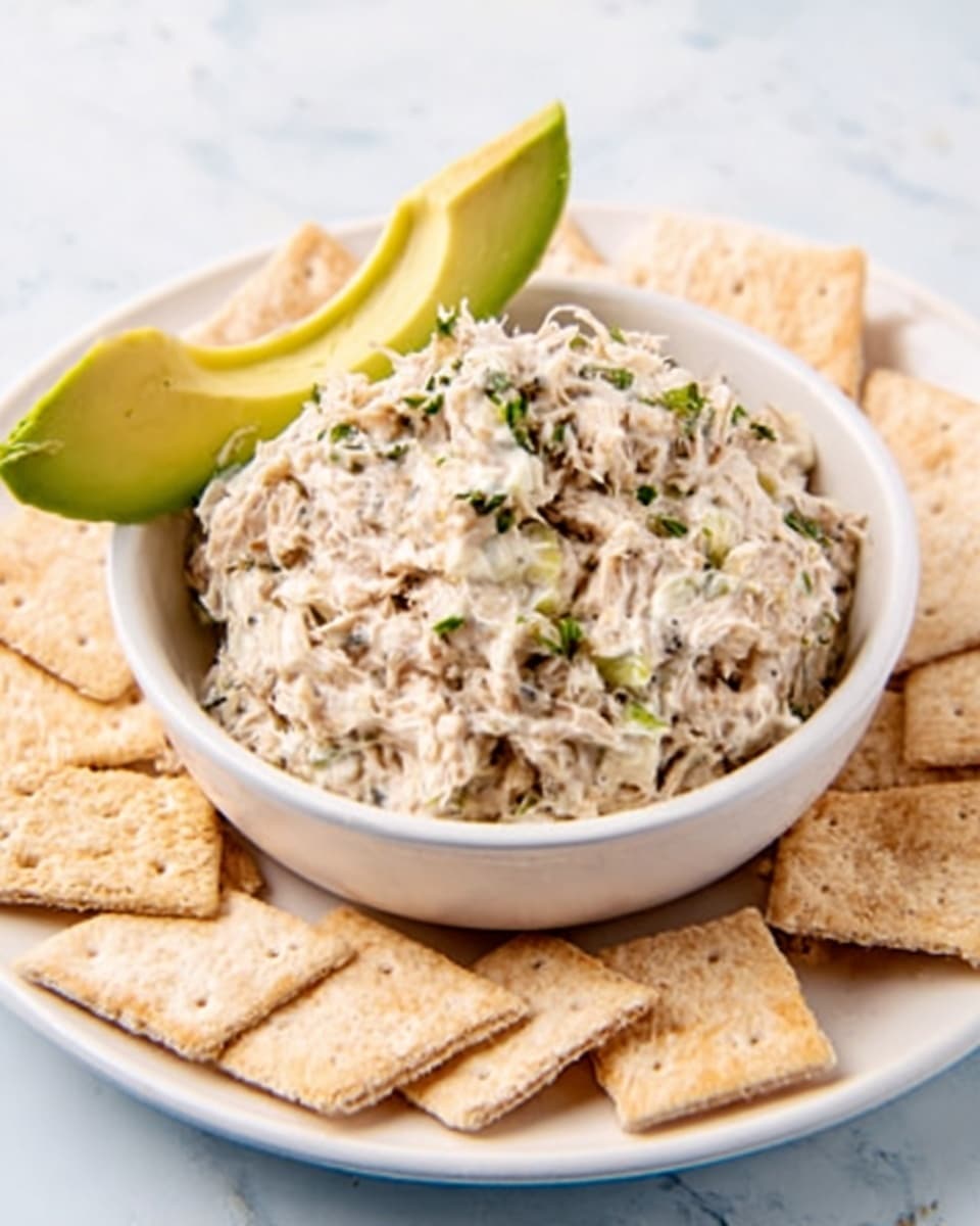 The image shows a beige bowl filled with a creamy, white mixture that looks like a chicken salad, dotted with small green herb bits and topped with fresh green dill on top. The bowl sits on a white marbled surface. To the left, there are a few green onion stalks placed diagonally, and in the bottom left corner, there is a small square wooden dish holding some coarse salt. To the top right, there are pieces of toasted bread with grill marks on a light tan wooden board. A wooden fork rests inside the bowl with a woman's hand reaching from the right side, about to scoop some salad. Photo taken with an iphone --ar 4:5 --v 7