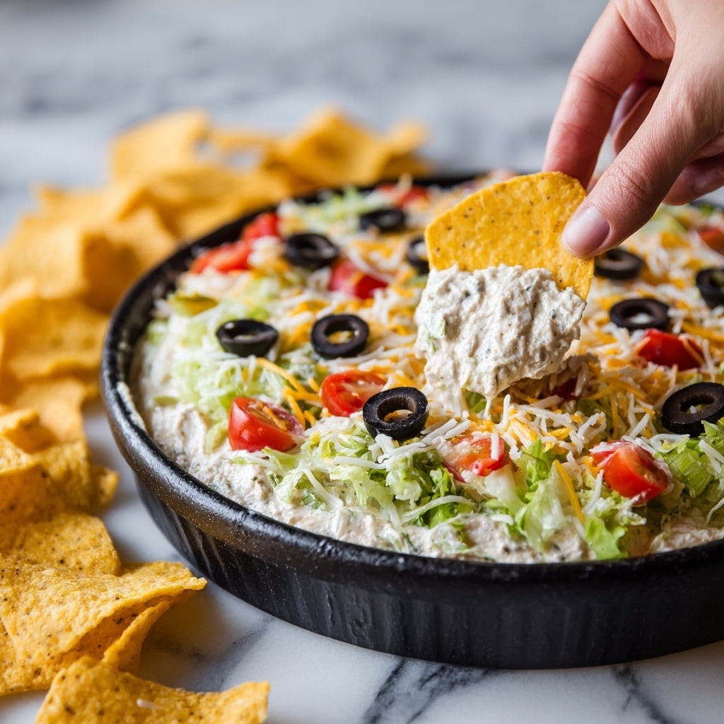A black round bowl filled with a colorful layered salad sits in the middle of a white marbled surface. The bottom layer is light green chopped lettuce, topped with a scattering of red cherry tomato pieces and yellow corn kernels. There are also dark red kidney beans and black olive slices spread evenly on top. The final layer is a light sprinkle of shredded white and yellow cheese. Around the black bowl, there is a ring of bright orange triangular tortilla chips. A spoon rests inside the bowl on the right side. Photo taken with an iphone --ar 4:5 --v 7