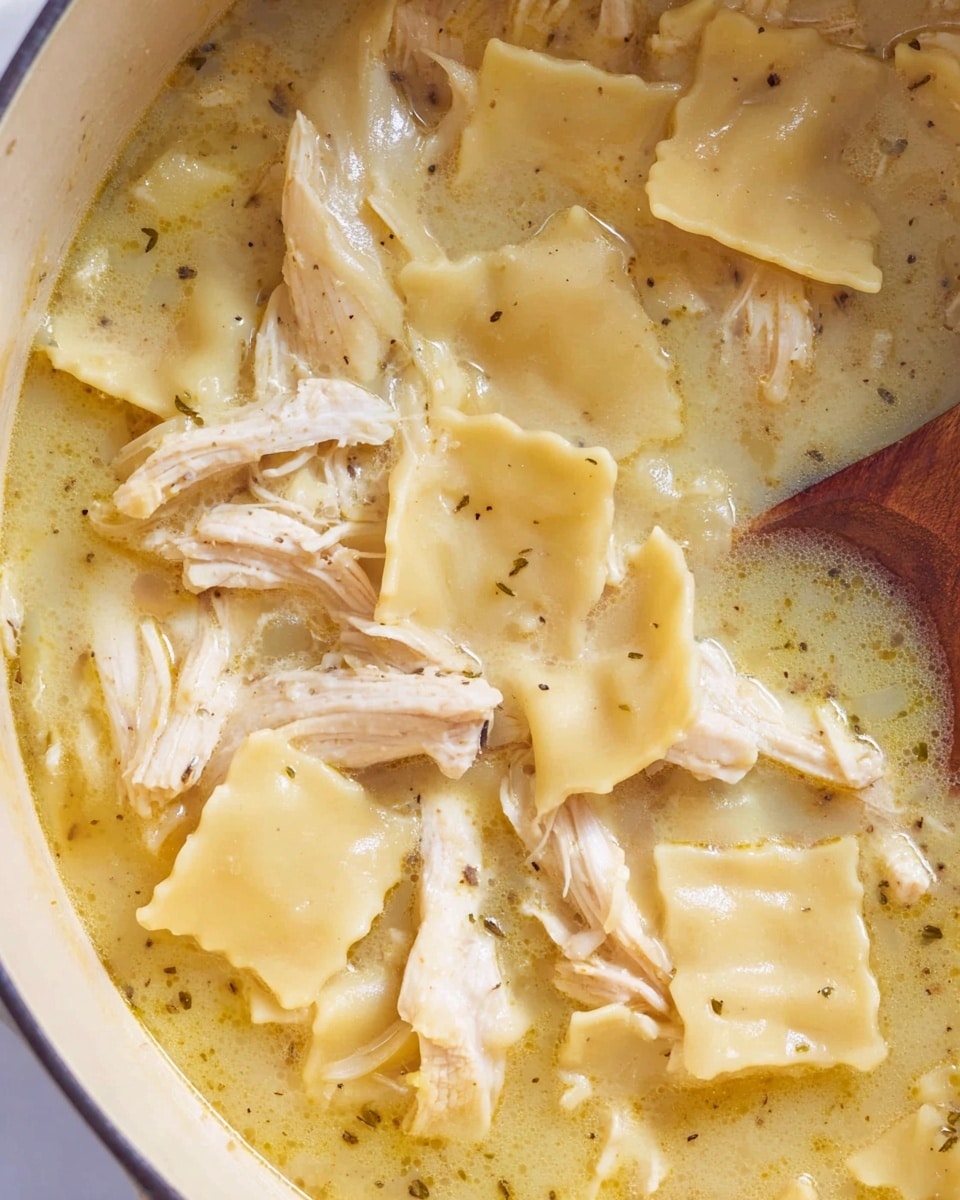 The image shows a close-up of a pot filled with a creamy chicken noodle soup. The soup has three main layers: the bottom layer is a light yellow broth with a smooth texture, the middle layer contains large, soft, square pasta pieces in a pale yellow color that float on the surface, and the top layer has shredded white chicken meat mixed evenly throughout. Small black pepper specks are scattered on top, and a wooden spoon is partially submerged in the soup on the right side. Photo taken with an iphone --ar 4:5 --v 7