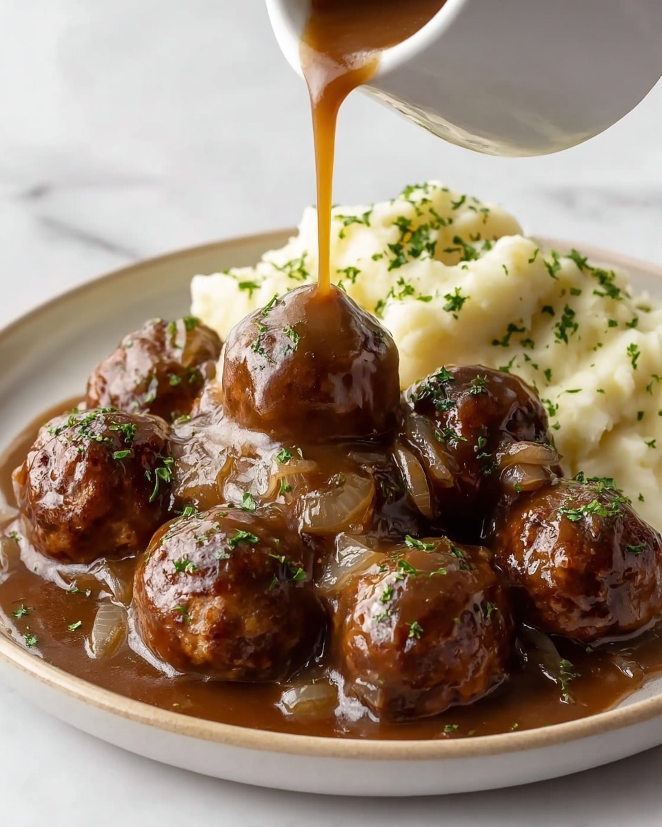 A white bowl holds a meal with two main layers: a base layer of creamy, smooth mashed potatoes with soft peaks, taking up about half the bowl, and on top, several round meatballs coated in a shiny, rich brown gravy filled with translucent, cooked onion slices. The meatballs are sprinkled with small bits of bright green chopped parsley. Nearby, a clear glass with iced tea and ice cubes sits on a beige cloth, all set on a white marbled surface. photo taken with an iphone --ar 4:5 --v 7