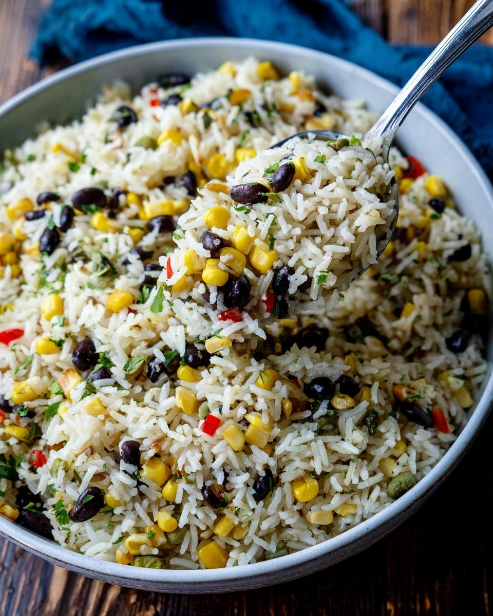 A close-up view of a large white bowl filled with cooked white rice mixed with yellow corn kernels, black beans, small green herbs, and tiny red pepper pieces, all evenly spread throughout the rice. A silver spoon lifts a portion of the rice mixture, showing a mix of all ingredients clearly. The bowl is placed on a dark wooden surface with a blue cloth partially visible in the top corner. The photo taken with an iphone --ar 4:5 --v 7