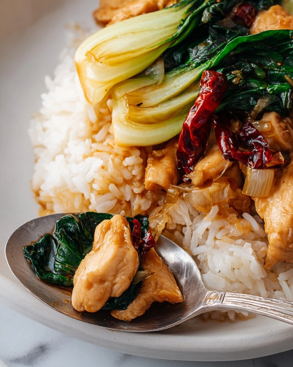 A white bowl holds two main parts: on the left side, a colorful stir-fry with brown glazed chicken pieces, bright green bok choy, dark green leafy vegetables, and pieces of dried red chili peppers in a shiny brown sauce; on the right side, a neat mound of white rice with a soft, grainy texture. The sauce pools slightly at the bottom, adding a glossy look to the ingredients. Another similar bowl is partly visible in the background, with the dish arranged in the same way. The bowls sit on a white marbled surface. photo taken with an iphone --ar 4:5 --v 7