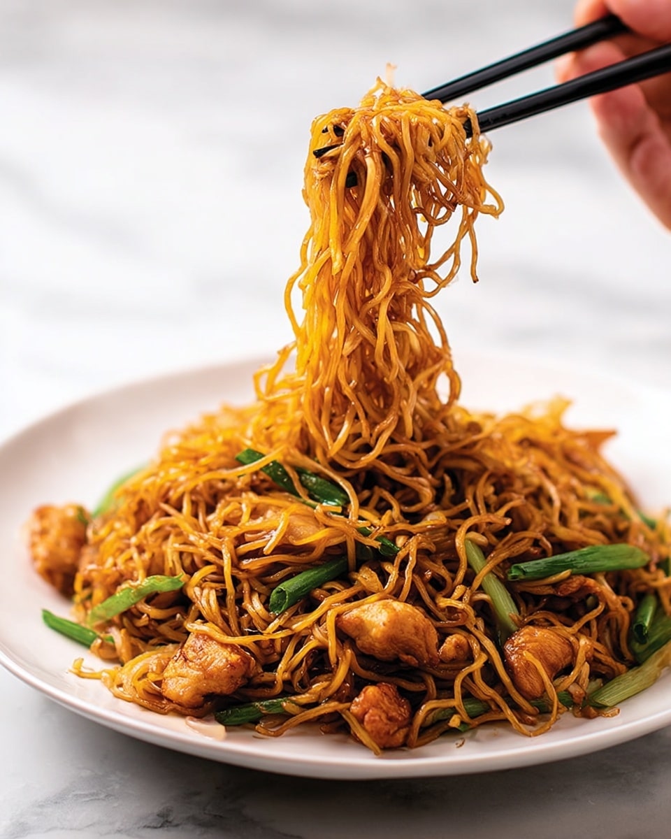 Two white plates are each filled with a serving of stir-fried noodles mixed with pieces of cooked chicken and bright green sliced scallions. The noodles are golden-brown and slightly crispy, tangled in a loose pile on each plate. The chicken pieces are browned and scattered evenly throughout the noodles, giving a slightly juicy texture. The bright green scallions add a fresh pop of color on top. Each plate has a pair of chopsticks resting diagonally on the edge, one pair is dark brown wood and the other is black. The background is a white marbled texture, adding a clean and simple setting. Photo taken with an iphone --ar 4:5 --v 7