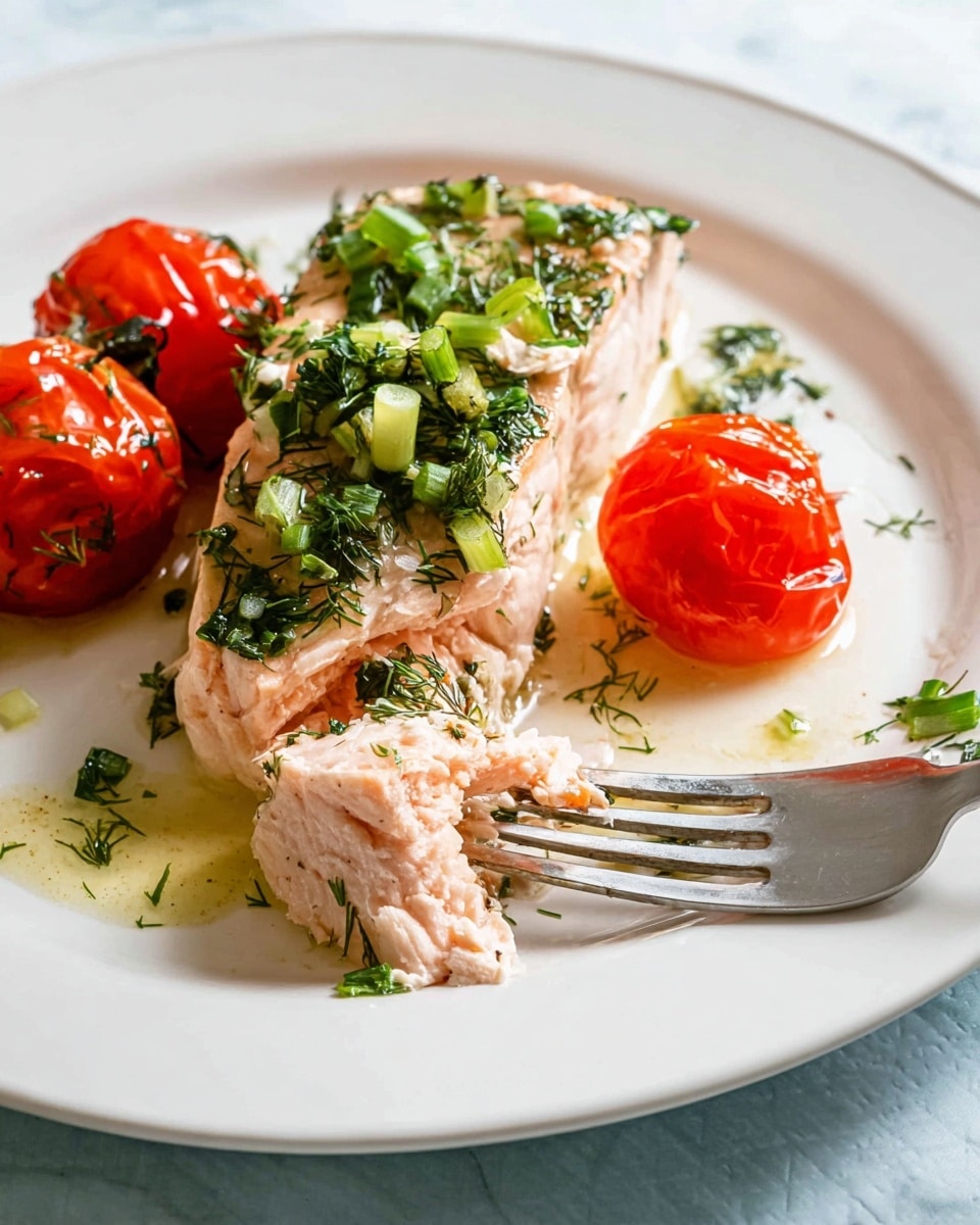 A white plate holds a piece of cooked salmon topped with chopped green herbs and green onion pieces, with two roasted bright red cherry tomatoes resting beside it. The salmon is light pink with a slightly flaky texture, and a small chunk of the fish is pierced by a silver fork in front of the main piece. There is a bit of light oil or sauce pooling around the salmon, and some scattered herbs add detail to the plate. The plate is set on a white marbled surface. Photo taken with an iphone --ar 4:5 --v 7