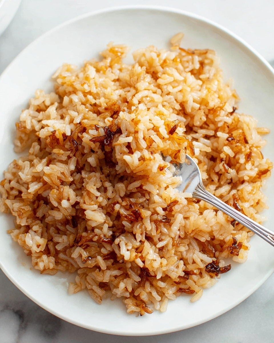 There is a close-up of a white plate filled with cooked rice that is golden brown with darker toasted bits mixed in. The rice grains are separate but sticky, showing a glossy texture and some slight crunchiness from the browned edges. A silver fork lifts a scoop of the rice from the center of the plate. The whole scene is set on a white marbled surface. photo taken with an iphone --ar 4:5 --v 7