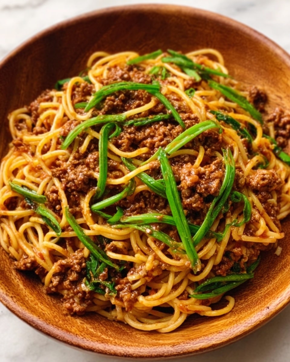 The image shows a round wooden bowl filled with cooked spaghetti noodles tangled in a mix of ground meat and bright green vegetable strips on top. The pile has a rich brown color from the meat sauce, with the green strips standing out, thin and curved, placed evenly across the top and mixed throughout. The noodles beneath are golden yellow and slightly glossy, with some strands peeking out from under the toppings. The bowl is set on a white marbled surface. Photo taken with an iphone --ar 4:5 --v 7