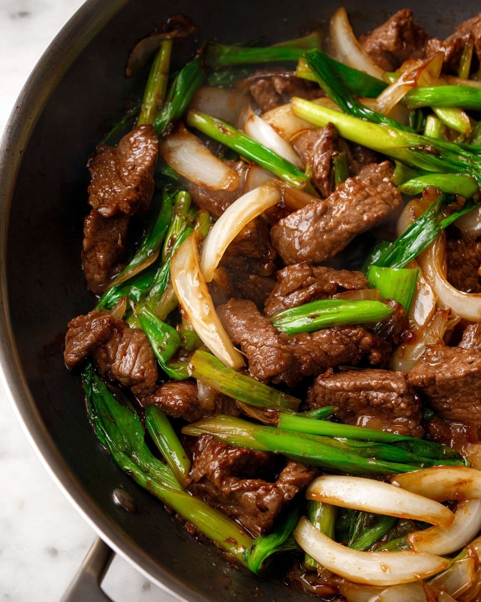 The image shows a white plate filled with stir-fried beef and vegetables. The dish has three main layers: thick slices of dark brown beef on top, mixed with wide pieces of soft light yellow and white onion strips scattered throughout. Bright green parts of scallions add fresh color, mixing with the meat and onions in the middle and bottom layers. The sauce is glossy brown, coating all the ingredients and pooling lightly at the bottom, giving the food a juicy look. The plate is placed on a woven mat with a pair of brown chopsticks in the background, all set against a white marbled texture surface. Photo taken with an iphone --ar 4:5 --v 7