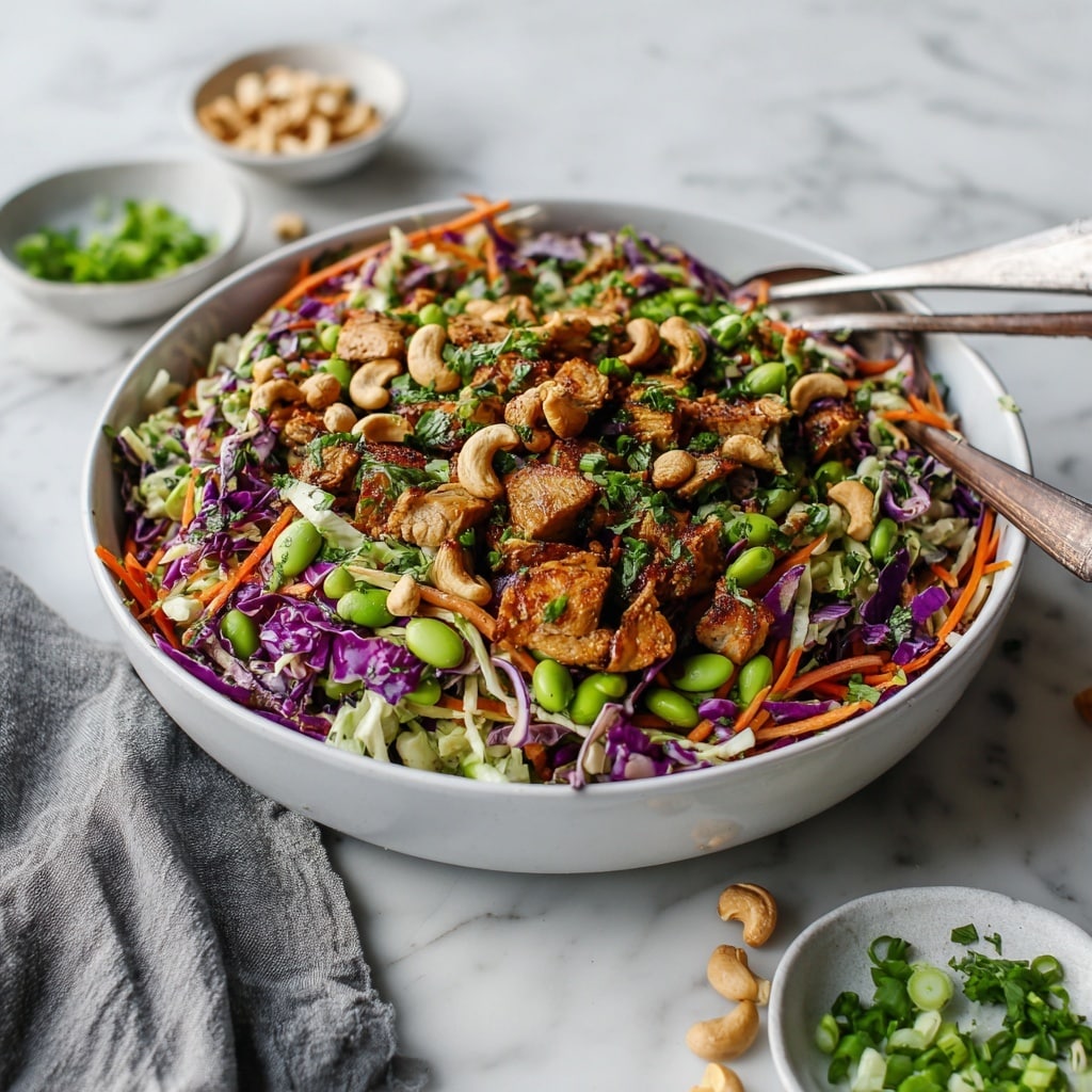 A large white bowl filled with a colorful salad made of several layers including shredded purple cabbage, orange shredded carrots, bright green edamame beans, chopped fresh herbs, chunks of cooked chicken, and whole cashew nuts, all mixed together with a fresh and textured look. In the background, two more white bowls hold additional ingredients, one with more cashew nuts and the other piled with shredded carrots and greens. A clear glass jar with a white dressing or sauce sits nearby, all placed on a surface with a white marbled texture. Photo taken with an iphone --ar 4:5 --v 7