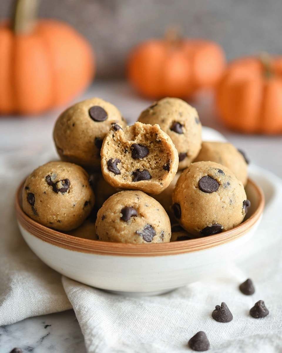 A close-up view of small, round cookie dough balls mixed with dark chocolate chips, placed in a white bowl with a light peach rim. The cookie dough balls are golden brown with a slightly rough texture, and the dark chocolate chips are embedded unevenly on the surface. The bowl sits on a white napkin, set against a white marbled texture background. photo taken with an iphone --ar 4:5 --v 7
