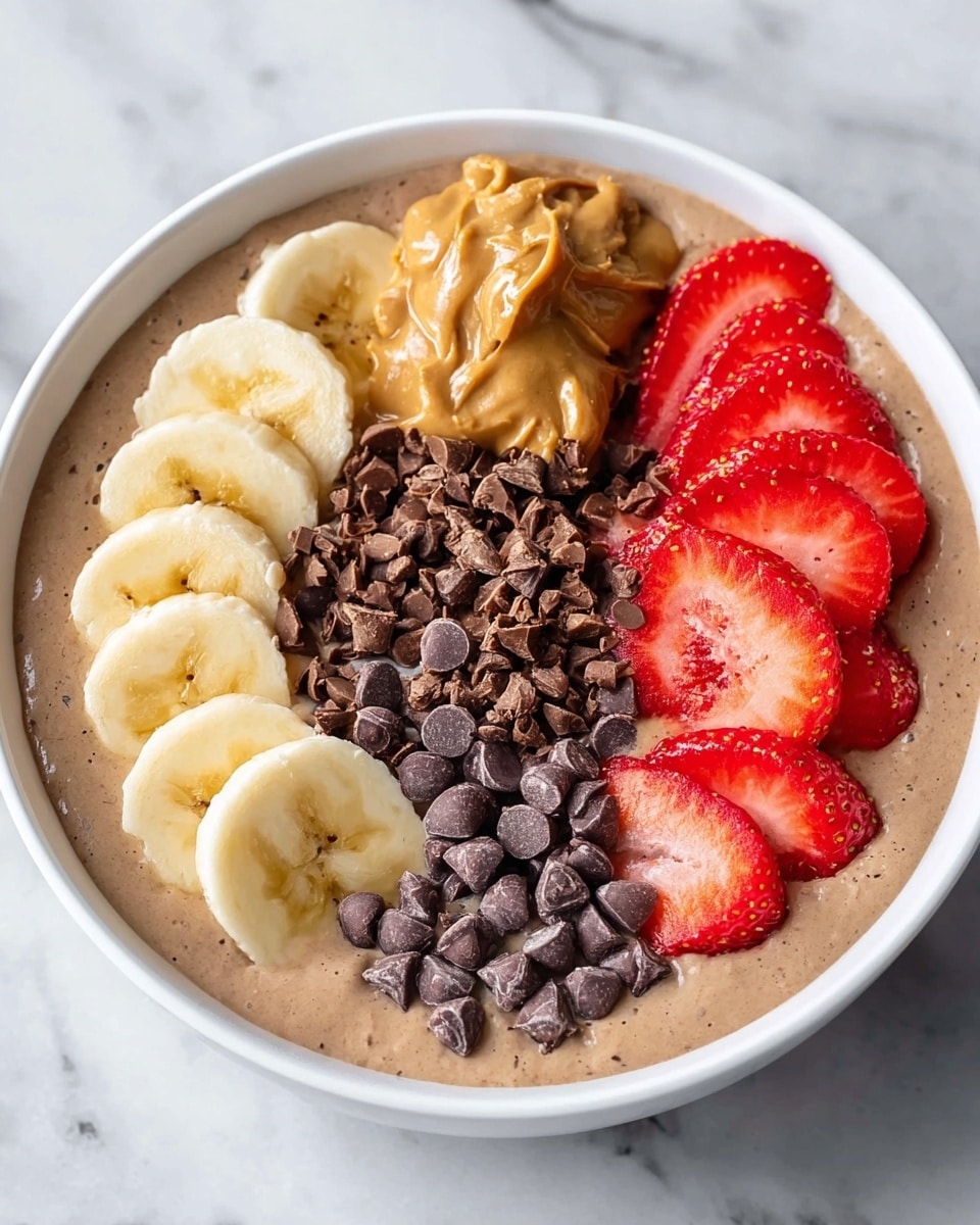 A white bowl filled with a thick, light brown smoothie base topped with five sections of ingredients arranged side by side. The first section features several round, pale yellow banana slices with a smooth texture. Next to it is a dollop of chunky, light brown peanut butter. In the middle, there is a small pile of shiny, dark brown chocolate chips, followed by a small heap of finely chopped darker chocolate pieces. The last section has multiple bright red strawberry slices with visible seeds and juicy texture. The bowl is placed on a white marbled surface. photo taken with an iphone --ar 4:5 --v 7